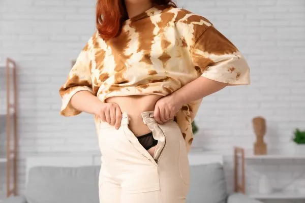 Image of woman trying to do her trousers up after pregnancy weight gain Olney